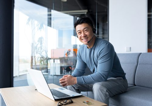 portrait of happy asian call center worker, man smiling and happy working with headset and computer, remote work, video call, online help