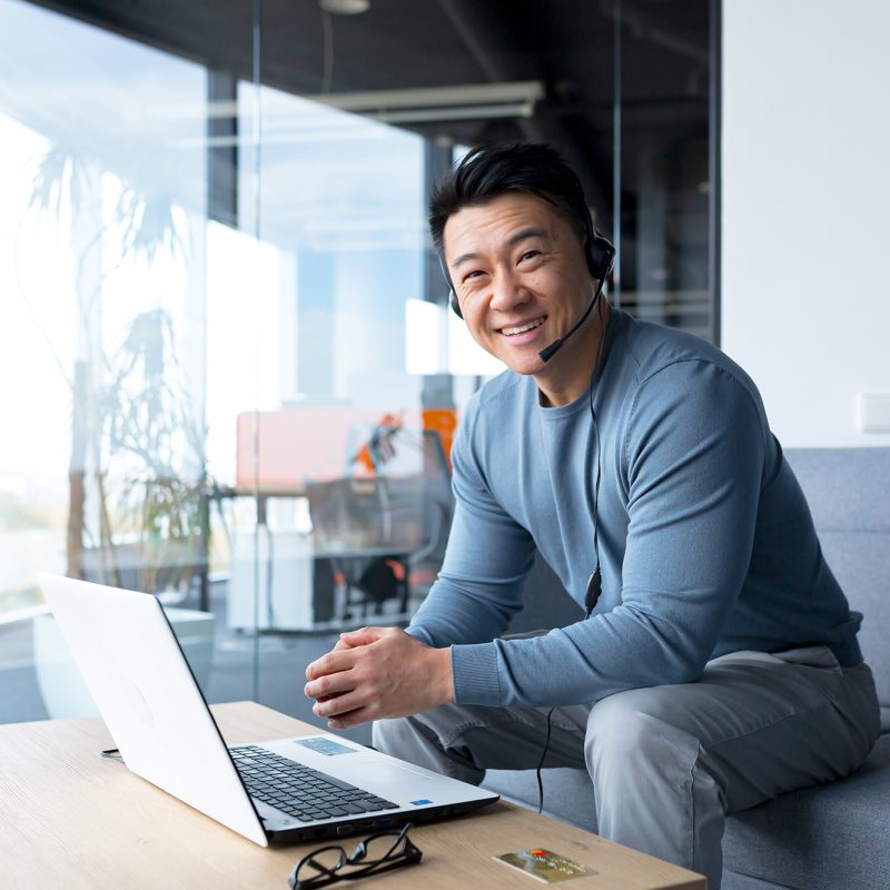 portrait of happy asian call center worker, man smiling and happy working with headset and computer, remote work, video call, online help